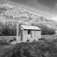 Load image into Gallery viewer, Old Tin Hut, black and white photograph of a corrugated iron shed beneath the mountains at Hakatere Station, Canterbury, New Zealand.