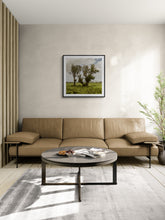 Load image into Gallery viewer, A modern living room scene featuring a light brown leather sofa, a round dark coffee table, a gray rug, and a framed landscape print by Stewart Nimmo