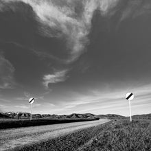 Load image into Gallery viewer, Open Road Signs, black and white photograph by Stewart Nimmo of a gravel road winding through the Canterbury high country near Lake Clearwater, New Zealand.