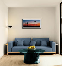 Load image into Gallery viewer, Barrytown Nikau Sunset panoramic landscape print farmed in black displayed in a modern living room with a blue couch
