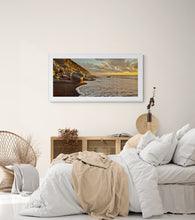 Load image into Gallery viewer, Warm evening light over rocks and waves Photographed by Stewart Nimmo at North Beach Cobden, West Coast New Zealand framed in white in modern bedroom