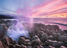 Load image into Gallery viewer, Punakaiki Blowholes at sunset with waves spraying over the rocks beneath a pink sky on the West Coast of New Zealand