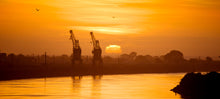 Load image into Gallery viewer, Golden sunset over Grey River and port cranes in Greymouth, West Coast New Zealand